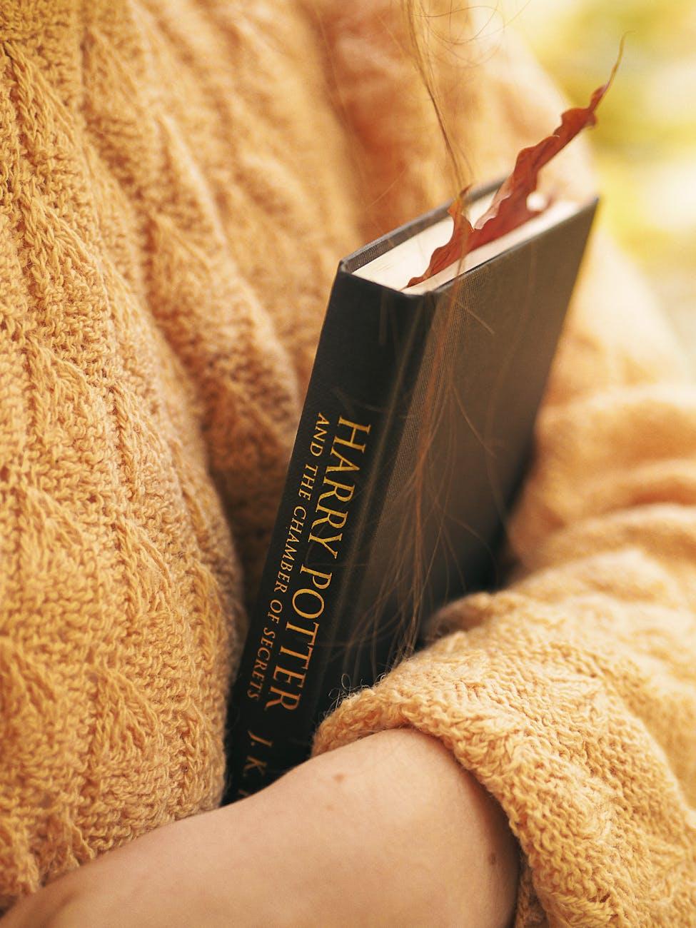 close up of woman in yellow sweater holding harry potter book with autumn leaf