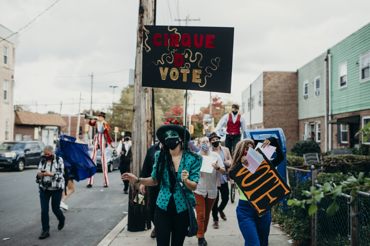 PHOTO unstoppable voters in a parade in circus costumes, some on stilts, holding signs that say VOTE and a sign reads CIRQUE D VOTE